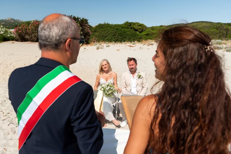der Standesbeamte mit obligatorischer Schärpe, die Übersetzerin sowie das Brautpaar während der Strandhochzeit - meer sardinien urlaub