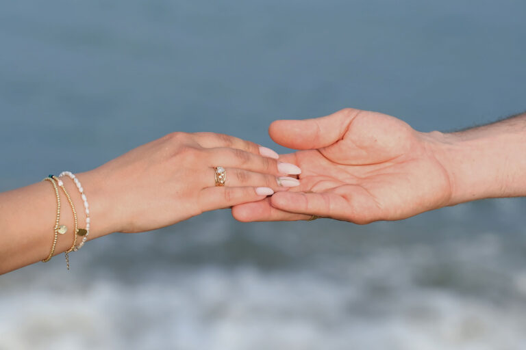 die-Hände-des-Brautpaares-während-einer-zarten-Berührung-vor-dem-Meer,-Strandhochzeit---meer-sardinien-urlaub