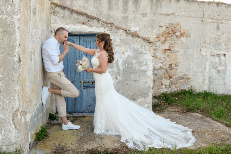 ein-eleganter-Handkuss-des-Bräutigams-vor-einem-malerischen,-alten-Gebäude-im-Anschluss-an-die-Strandhochzeit---meer-sardinien-urlaub