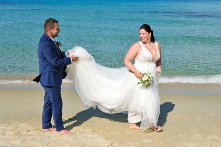 liebevoll hält der Bräutigam das Brautkleid beim kleinen Strandspaziergang nach der Strandhochzeit - meer sardinien urlaub
