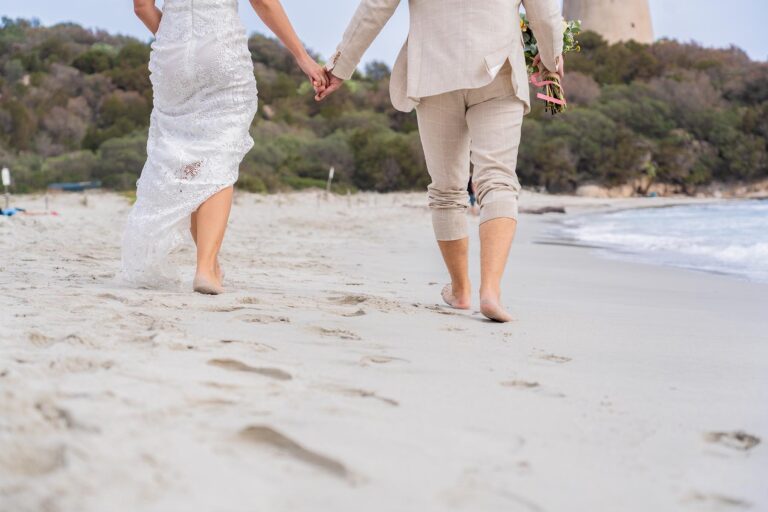 Brautpaar läuft barfuß am Strand entlang bei einer Hochzeit auf Sardinien