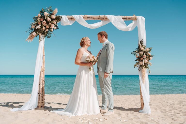 bezauberndes Bild des Brautpaares am Traubogen, Strandhochzeit - meer sardinien urlaub
