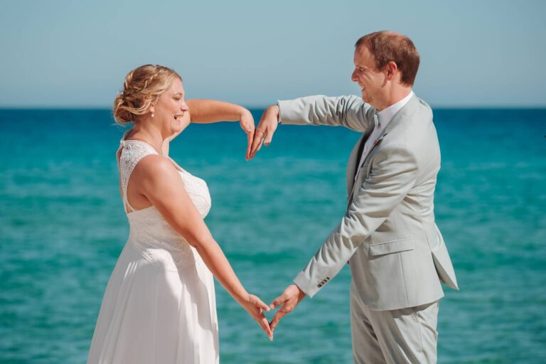 das oberglückliche Brautpaar formt ein großes Herz, Strandhochzeit - meer sardinien urlaub