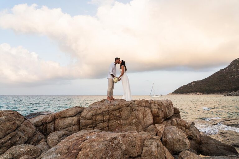 ein romantischer Kuß des Brautpaares auf den Felsen mit dem herrlichen Meer im Hintergrund, Strandhochzeit - meer sardinien urlaub