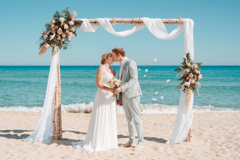 wunderschönes Paarbild am Traubogen unter einem Blütenregen, Strandhochzeit - meer sardinien urlaub