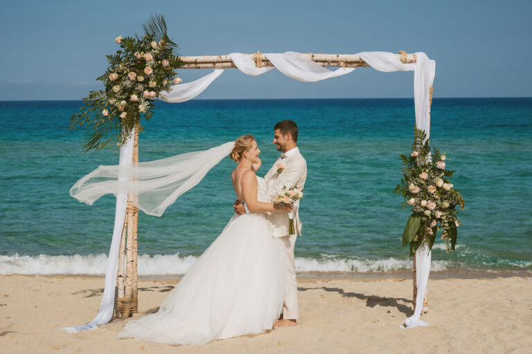 Braut-mit-wehendem-Schleier-und-Bräutigam-unter-dem-Traubogen,-Strandhochzeit---meer-sardinien-urlaub