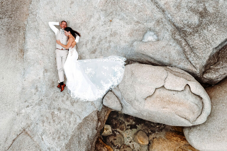Drohnen-Aufnahme-des-auf-einem-Felsen-liegenden-Brautpaares,-Strandhochzeit---meer-sardinien-urlaub