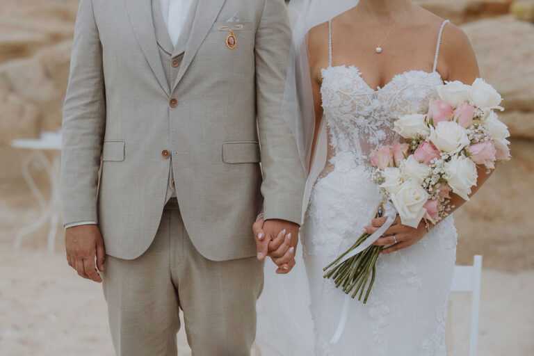 Hand-in-Hand-vernimmt-das-Brautpaar-die-Worte-der-Zeremonie-zur-Strandhochzeit---meer-sardinien-urlaub