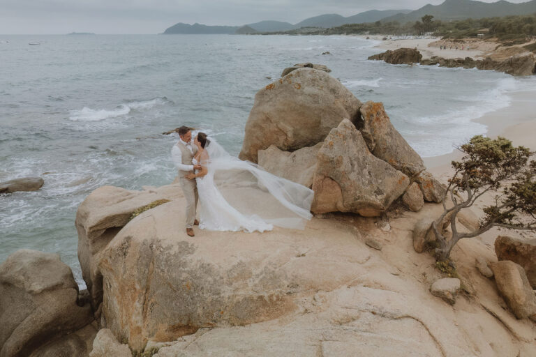 das-Brautpaar-auf-einem-Felsen-während-des-Paarshootings-nach-der-Strandhochzeit---meer-sardinien-urlaub