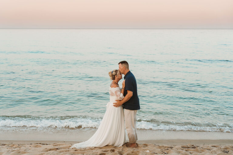 das-Brautpaar-in-inniger-Umarnung-vor-dem-glitzernden-Meer,-Strandhochzeit---meer-sa