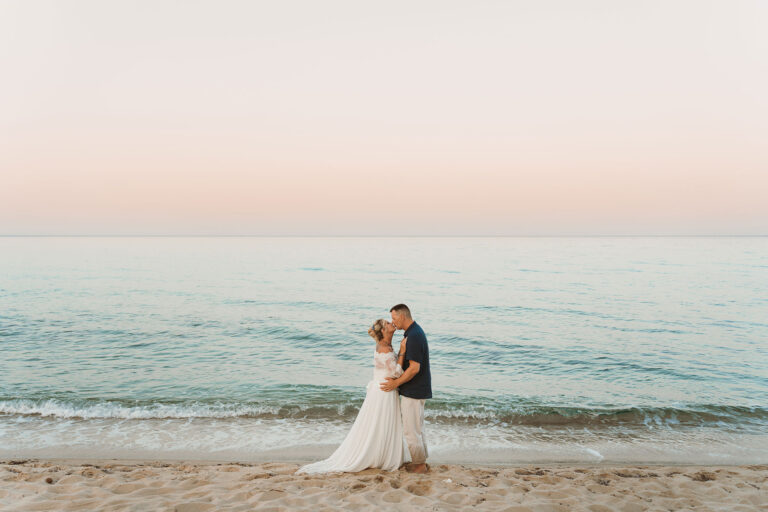 das-Brautpaar-küsst-sich-im-Abendlicht-vor-dem-glitzernden-Meer,-Strandhochzeit---meer-sardinien-urlaub