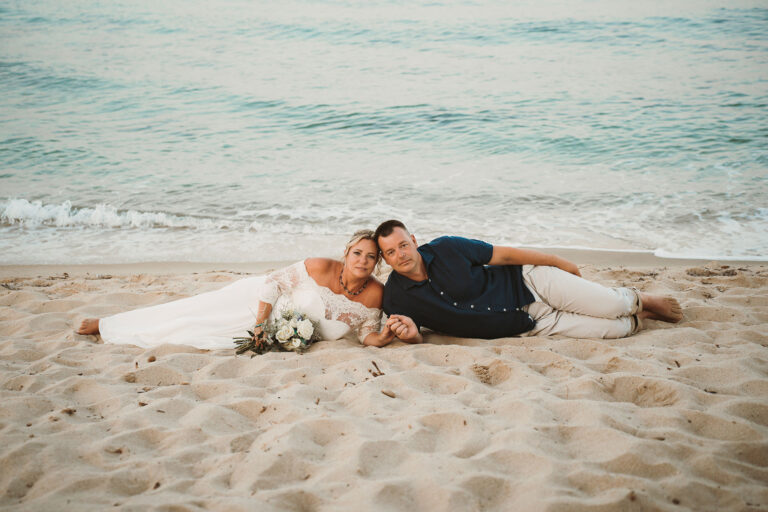 das-Paar-liegend-im-Sand-während-des-Paarshootings,-Strandhochzeit---meer-sardinien-urlaub