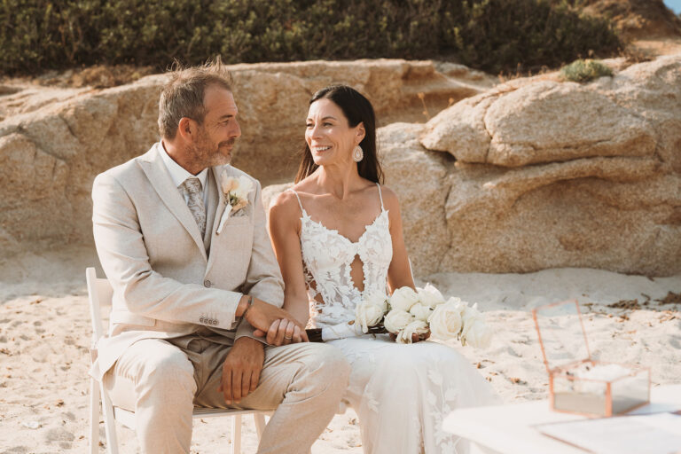 das-sitzende-Brautpaar-während-der-Strandhochzeit---meer-sardinien-urlaub