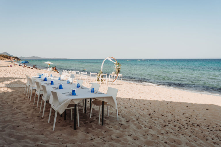 der-Tisch-für-die-anschliessende-Feier-und-der-Traubogen-im-Hintergrund,-Strandhochzeit---meer-sardinien-urlaub
