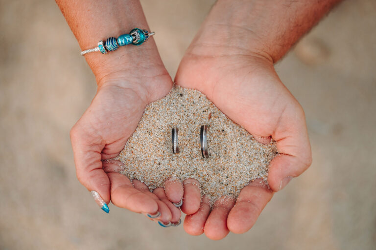 die-Hände-des-Brautpaares-halten-gemeinsam-den-Sand-mit-den-Trauringen,-Strandhochzeit---meer-sardinien-urlaub