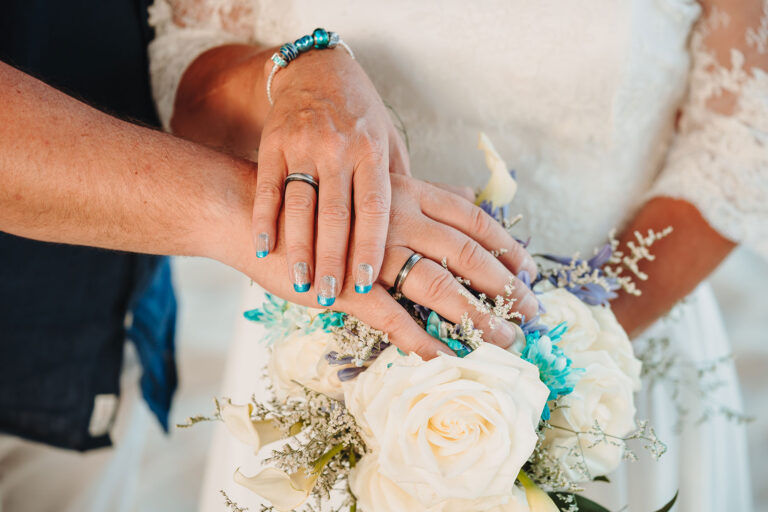 die-Hände-des-Brautpaares-mit-den-Trauringen-über-dem-Brautstrauss,-Strandhochzeit---meer-sardinien-urlaub