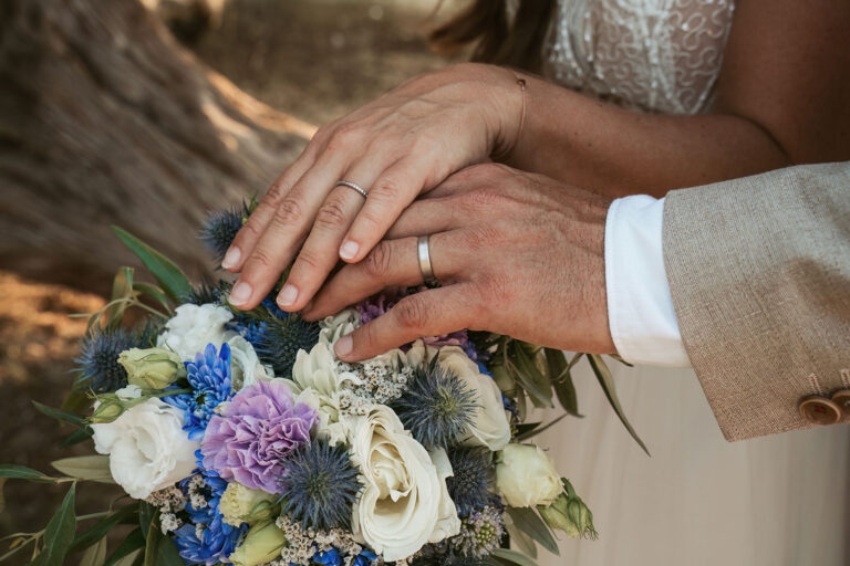 die-Hände-des-Brautpaares-mit-den-frischen-Eheringen-über-dem-Brautstrauss,-Strandhochzeit---meer-sardinien-urlaub