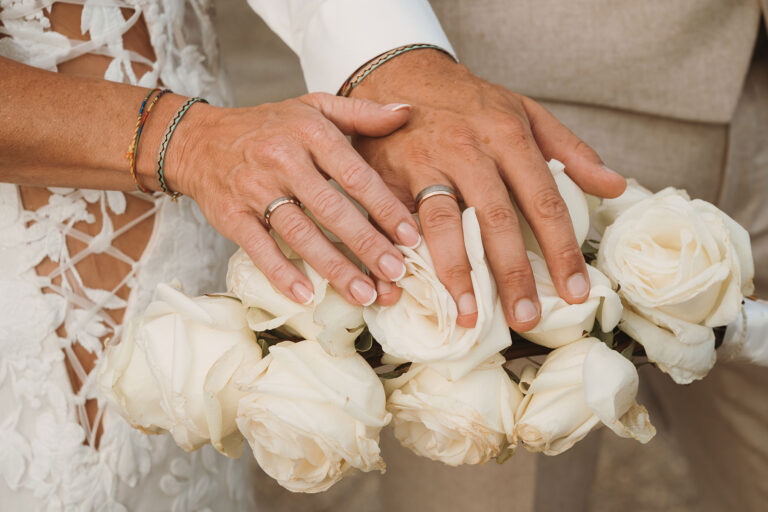 die-Hände-mit-den-glitzernden-Trauringen-ruhen-auf-dem-Brautstrauss,-Strandhochzeit---meer-sardinien-urlaub