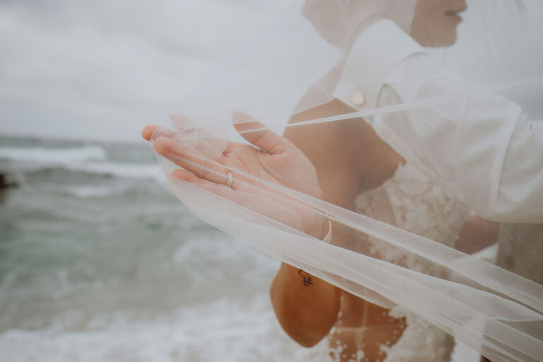 die-Hand-der-Braut-hält-ihren-Schleier-bei-der-Strandhochzeit---meer-sardinien-urlaub