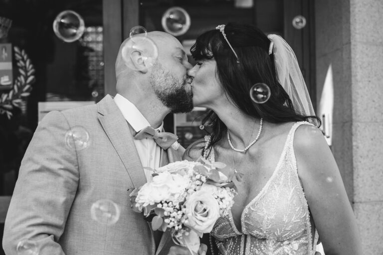 ein-Küsschen-begleitet-von-zahlreichen-Seifenblasen-vor-dem-Rathaus,-schwarz-weiss,-Trauung-im-Standesamt---meer-sardinien-urlaub