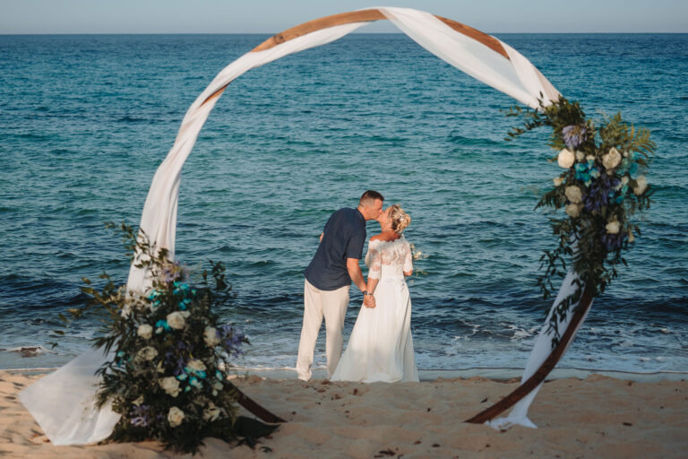 ein-Küsschen-hinter-dem-Traubogen,-Strandhochzeit---meer-sardinien-urlaub