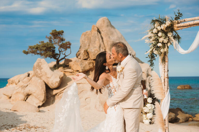 ein-Kuss-am-Traubogen-mit-dem-Felsen-im-Hintergrund,-Strandhochzeit---meer-sardinien-urlaub