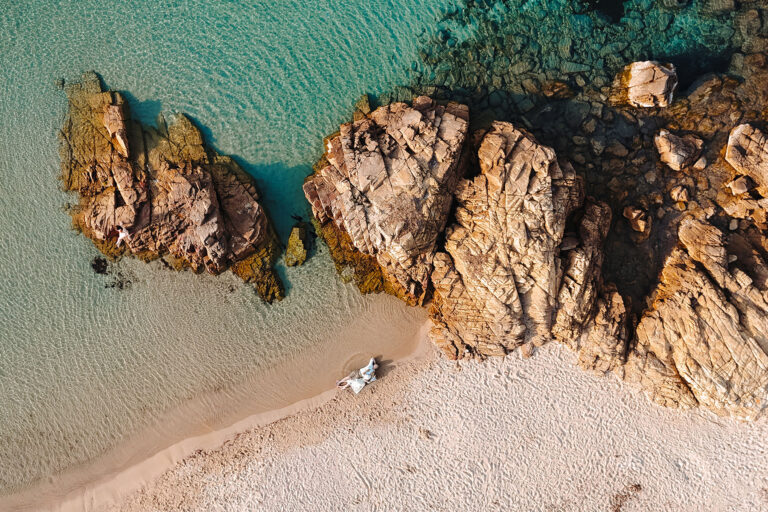 herrliche-Drohnenaufnahme-des-am-Ufer-liegenden-Brautpaares,-Strandhochzeit---meer-sardinien-urlaub