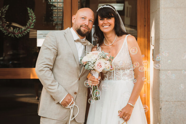 lächelnd-blickt-das-Brautpaar-vor-dem-Rathaus-in-die-Kamera,-Trauung-im-Standesamt---meer-sardinien-urlaub