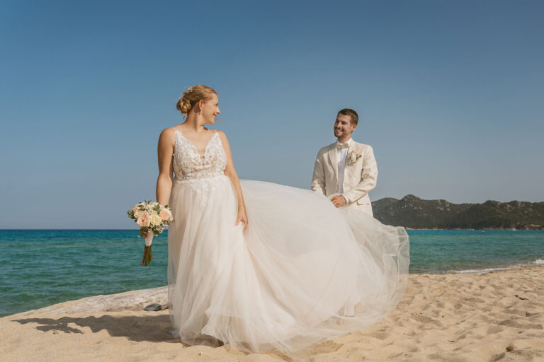 liebevoll-hebt-der-Bräutigam-das-Kleid-seiner-Braut,-Strandhochzeit---meer-sardinien-urlaub