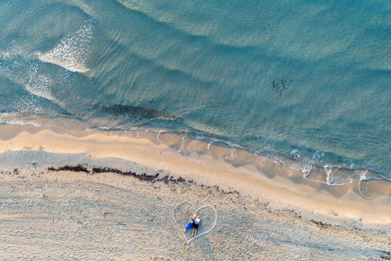 atemberaubende-Drohnenaufnahme-eines-liegenden,-von-einem-Herzen-eingerahmten-Paares-am-Strand,-Strandhochzeit---meer-sardinien-urlaub
