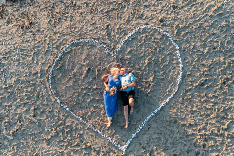 ein-aus-weißen-Steinen-geformtes-Herz-am-Strand-umgibt-das-küssende-Brautpaar,-Strandhochzeit---meer-sardinien-urlaub