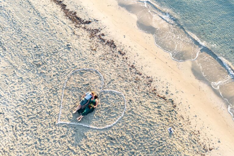 herrliche-Drohnenaufnahme-eines-in-einem-Herzen-am-Strand-liegenden-Paares,-Strandhochzeit---meer-sardinien-urlaub