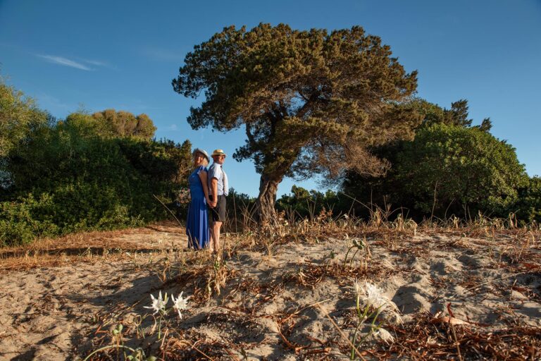 schönes-Paarbild-in-einem-Naturschauspiel-mit-Strandlilien-und-einem-imposanten-Wacholderbaum-am-Strand,-Strandhochzeit---meer-sardinien-urlaub