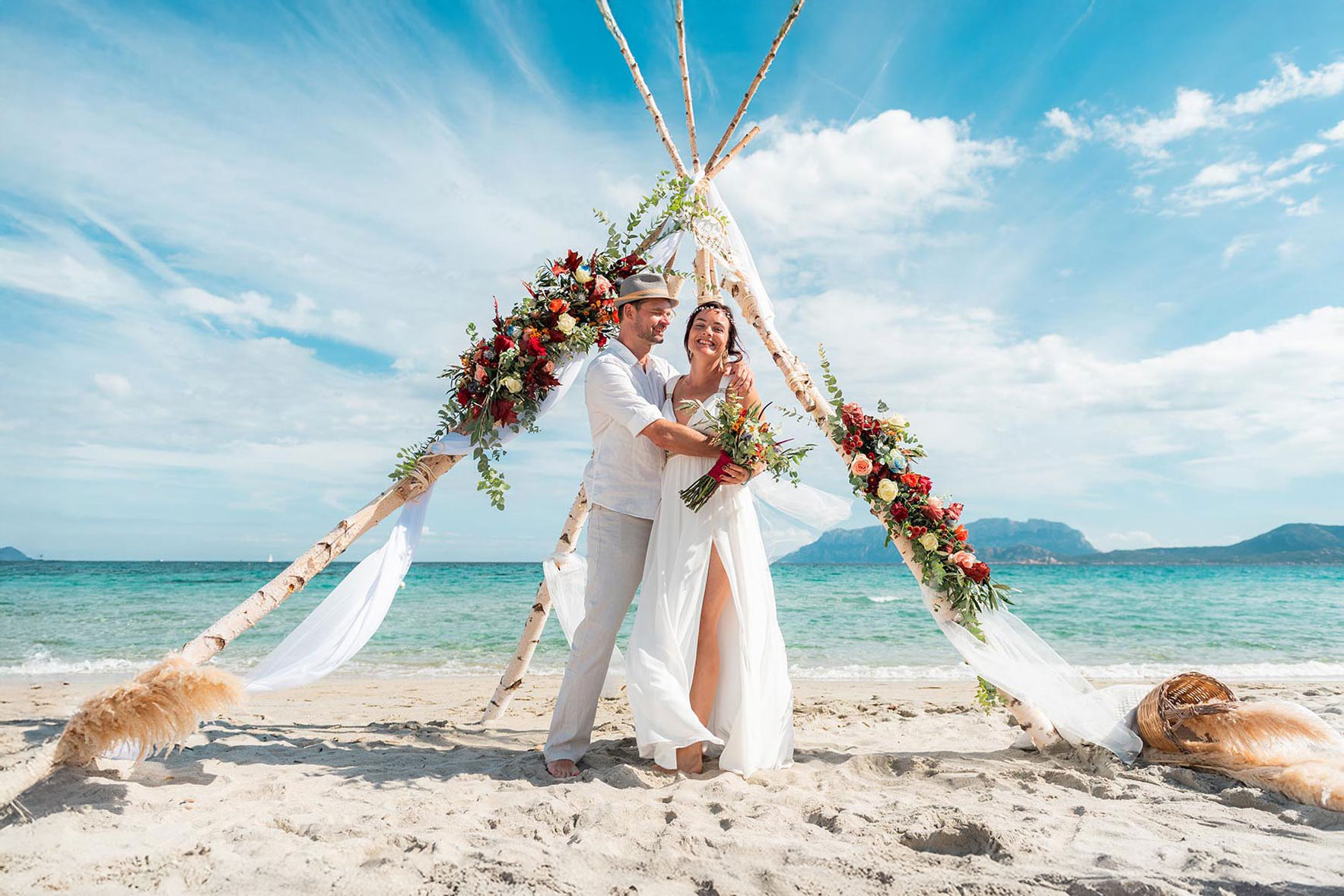 Strahlendes Brautpaar unter einem Traubogen am Strand bei einer Hochzeit auf Sardinien