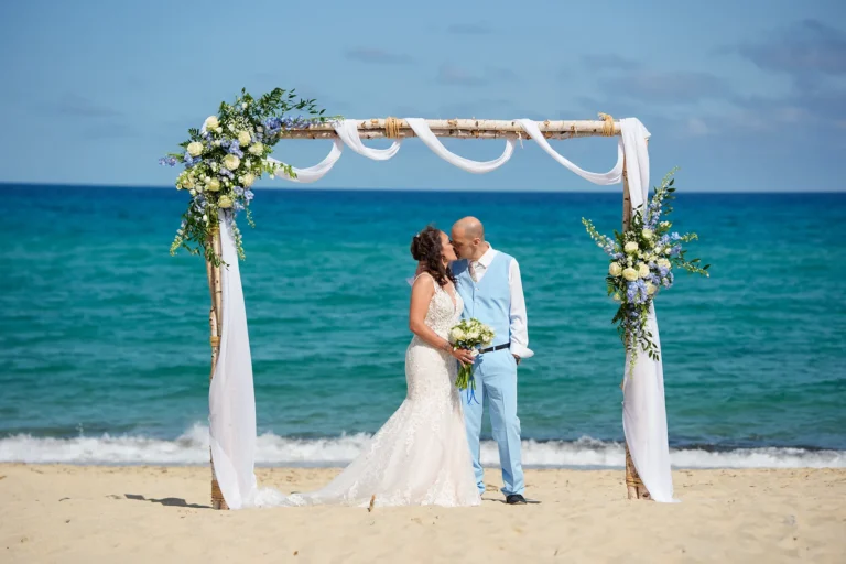 küssendes Paar vor dem Traubogen, Strandhochzeit - meer sardinien urlaub