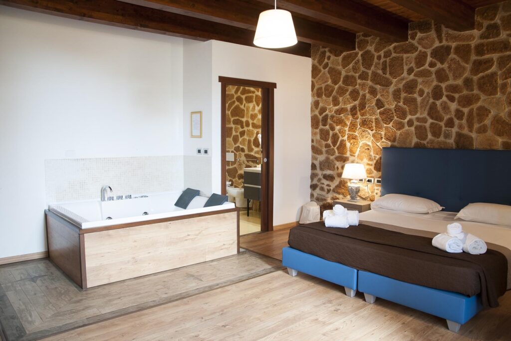 Eine schöne Steinwand ziert die Wand der grosszügigen Juniorsuite Prestige 201, Hotel Maison de Charme Bienestar, Alghero - meer sardinien urlaub