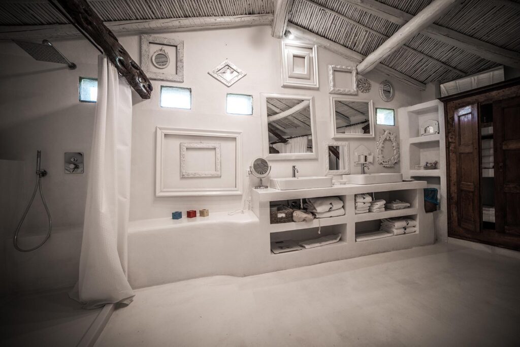 Das komplett weisse Bad im Kontrast zum farbenfrohen Schlafraum des Art-Suite-Studio-Zimmers des Su Gologone Experience Hotels, Oliena - meer sardinien urlaub